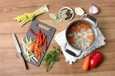 Pot of delicious vegetable bouillon and ingredients on wooden table, flat lay