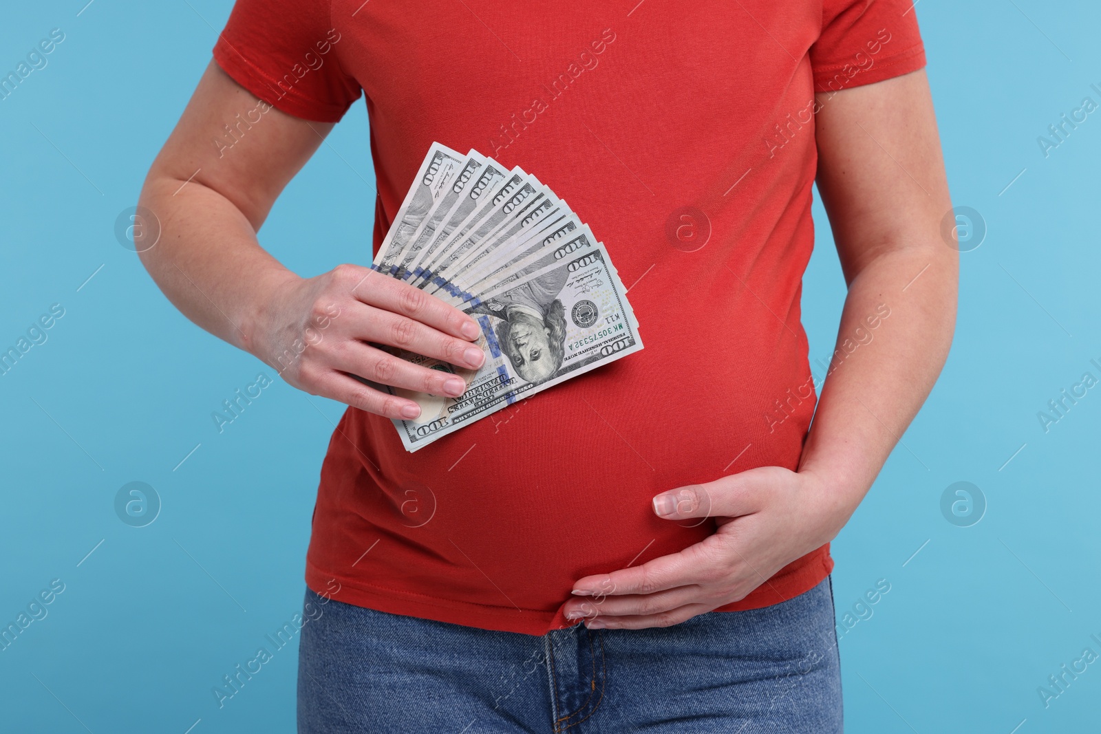 Photo of Surrogate mother. Pregnant woman with dollar banknotes on light blue background, closeup