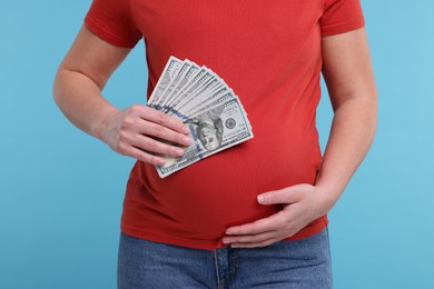 Photo of Surrogate mother. Pregnant woman with dollar banknotes on light blue background, closeup