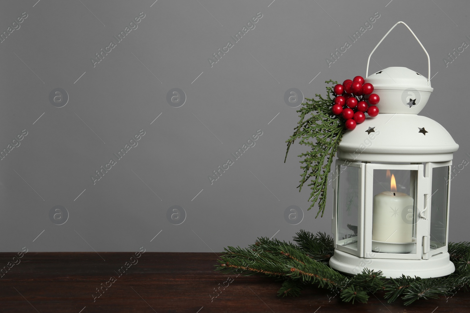 Photo of Christmas lantern decorated with coniferous twigs and berries on grey background, space for text