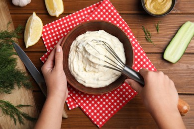 Woman making delicious tartar sauce at wooden table, top view