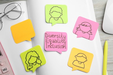 Photo of Sticky notes with words Diversity, Equality, Inclusion and drawings of people on wooden table, flat lay
