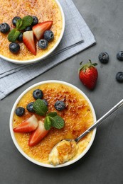 Delicious creme brulee with berries and mint in bowls on grey table, flat lay