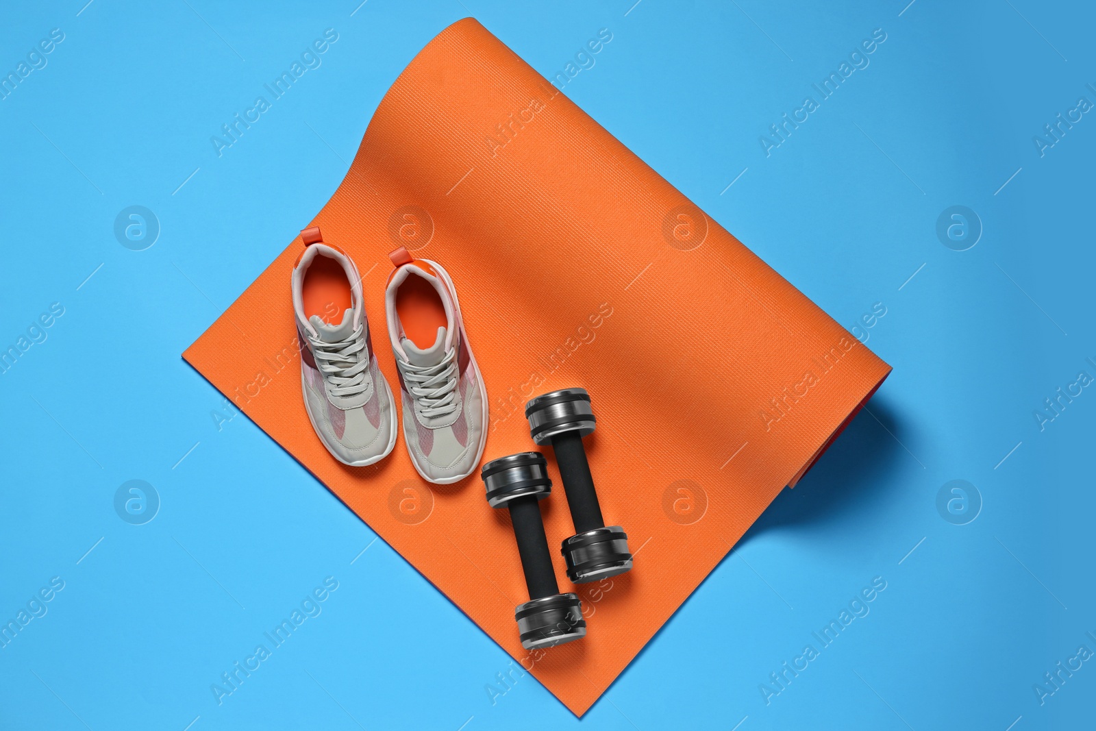 Photo of Exercise mat, dumbbells and shoes on turquoise background, flat lay