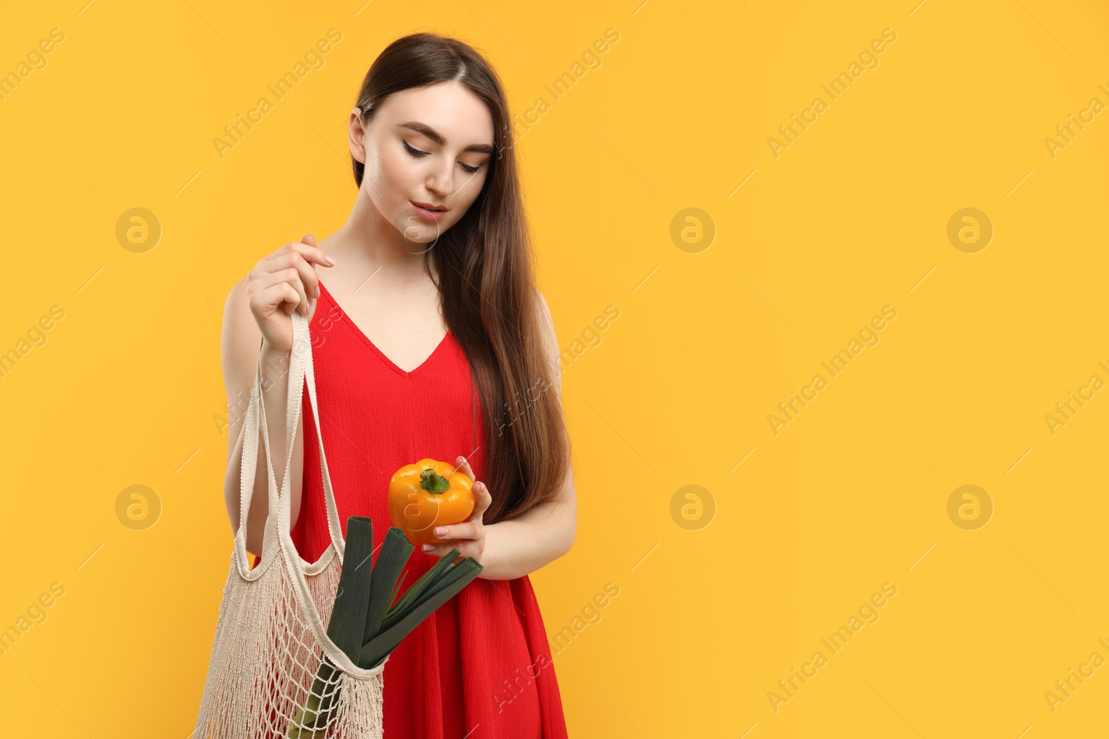 Photo of Woman with string bag of fresh vegetables on orange background, space for text