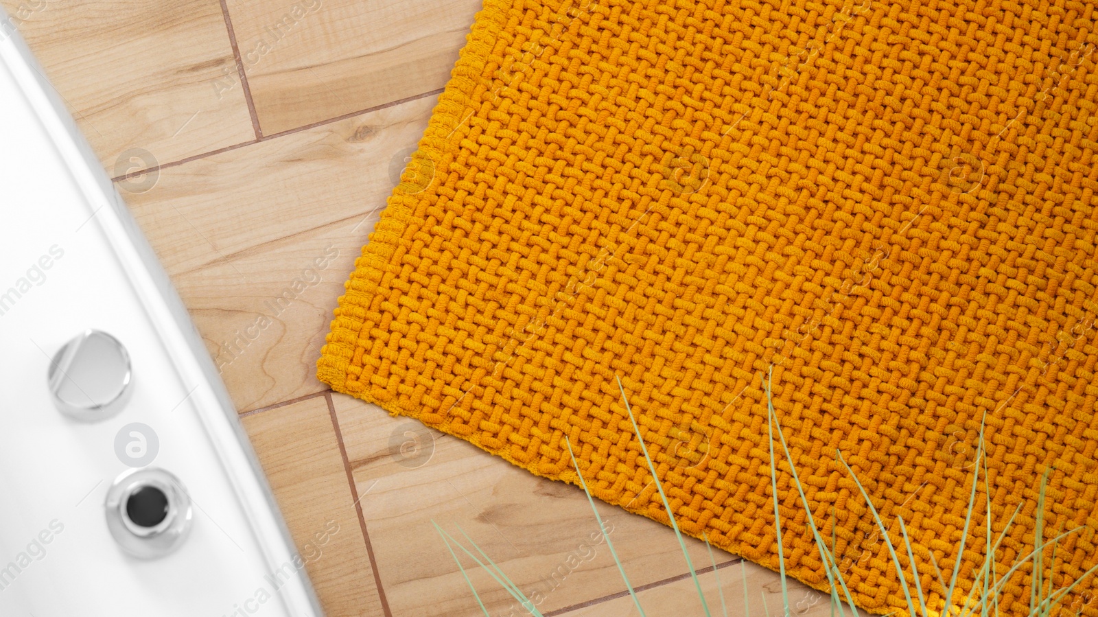 Photo of Soft mustard color bath mat near tub on wooden floor in bathroom, above view