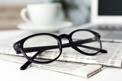Photo of Newspapers and glasses on white table indoors, closeup