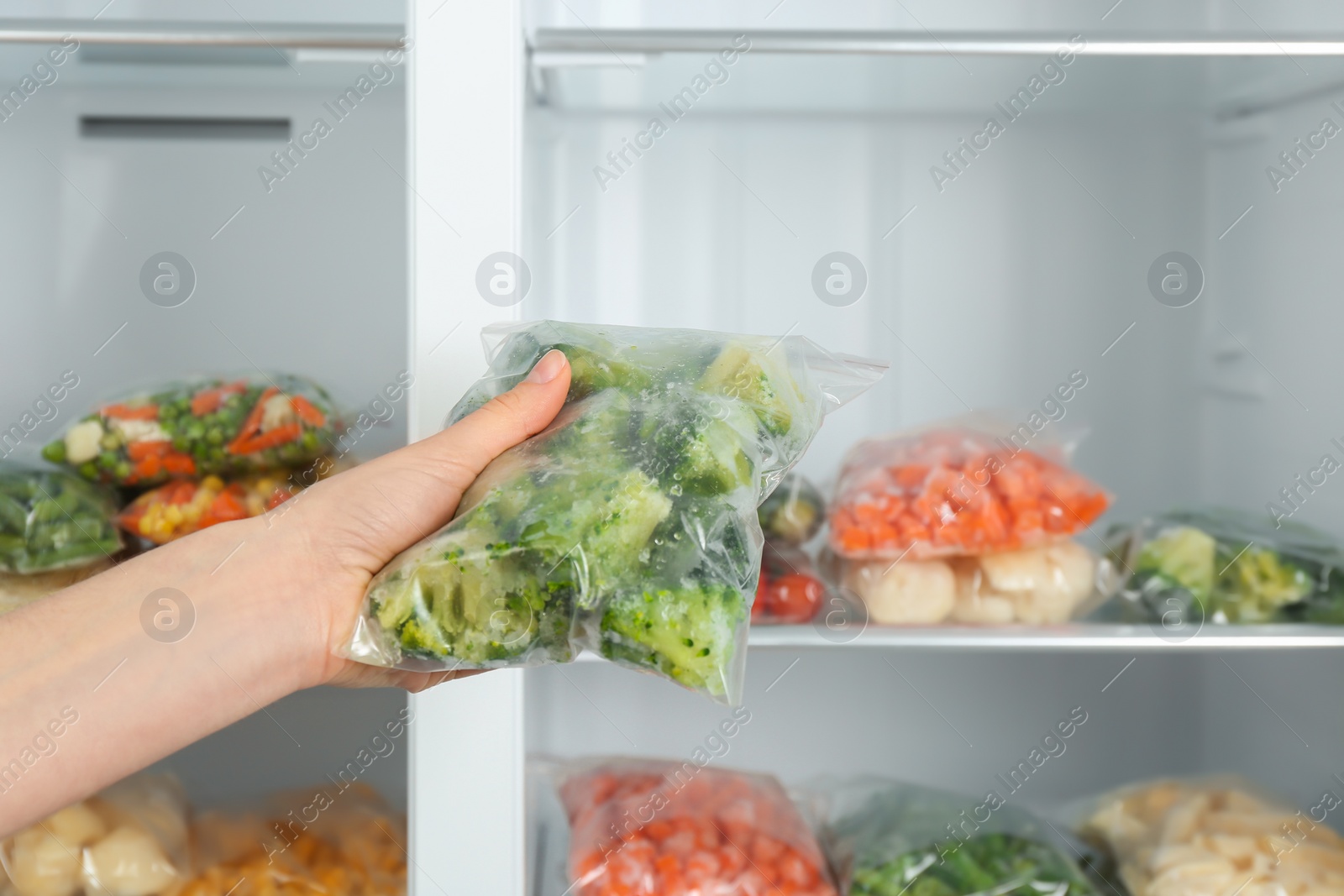 Photo of Woman holding plastic bag with frozen broccoli near open refrigerator, closeup