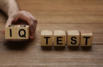 Photo of Man taking cubes with text IQ Test on wooden background, closeup