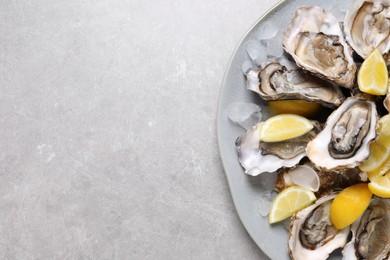 Photo of Fresh oysters with lemon and ice on grey table, top view. Space for text
