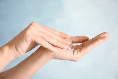 Woman applying hand cream on light background, closeup