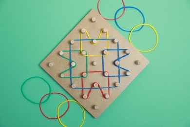 Photo of Wooden geoboard with rubber bands on green background, flat lay. Educational toy for motor skills development