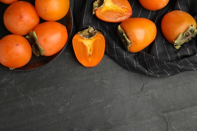Photo of Tasty ripe persimmons on black slate table, flat lay. Space for text