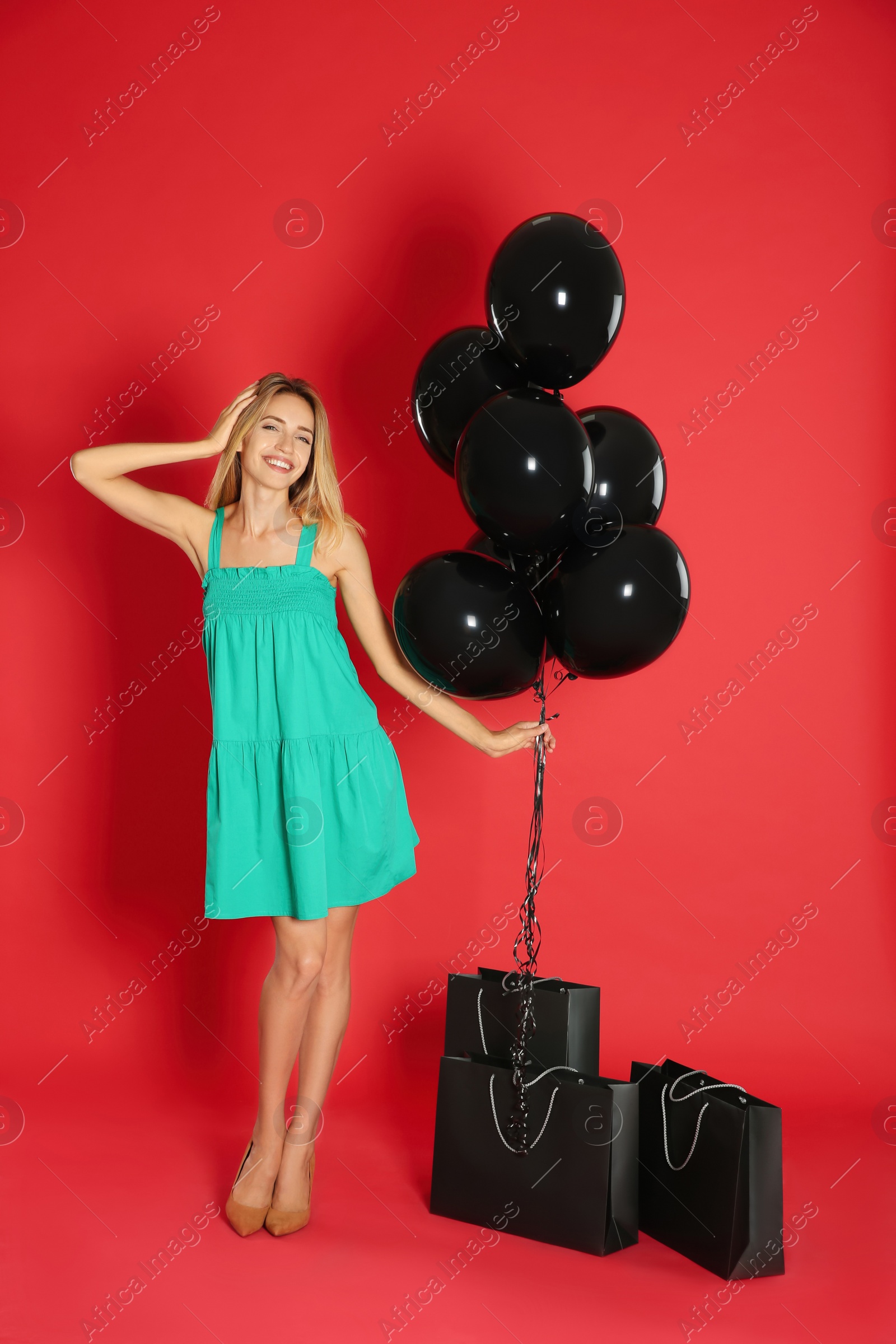 Photo of Happy young woman with balloons and shopping bags on red background. Black Friday Sale
