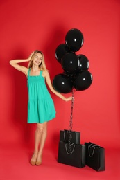 Happy young woman with balloons and shopping bags on red background. Black Friday Sale