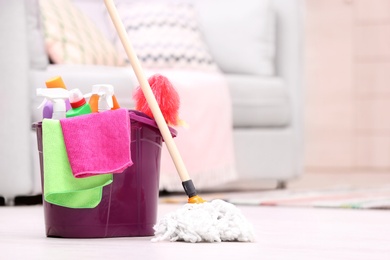 Photo of Bucket with cleaning supplies on floor indoors. Space for text