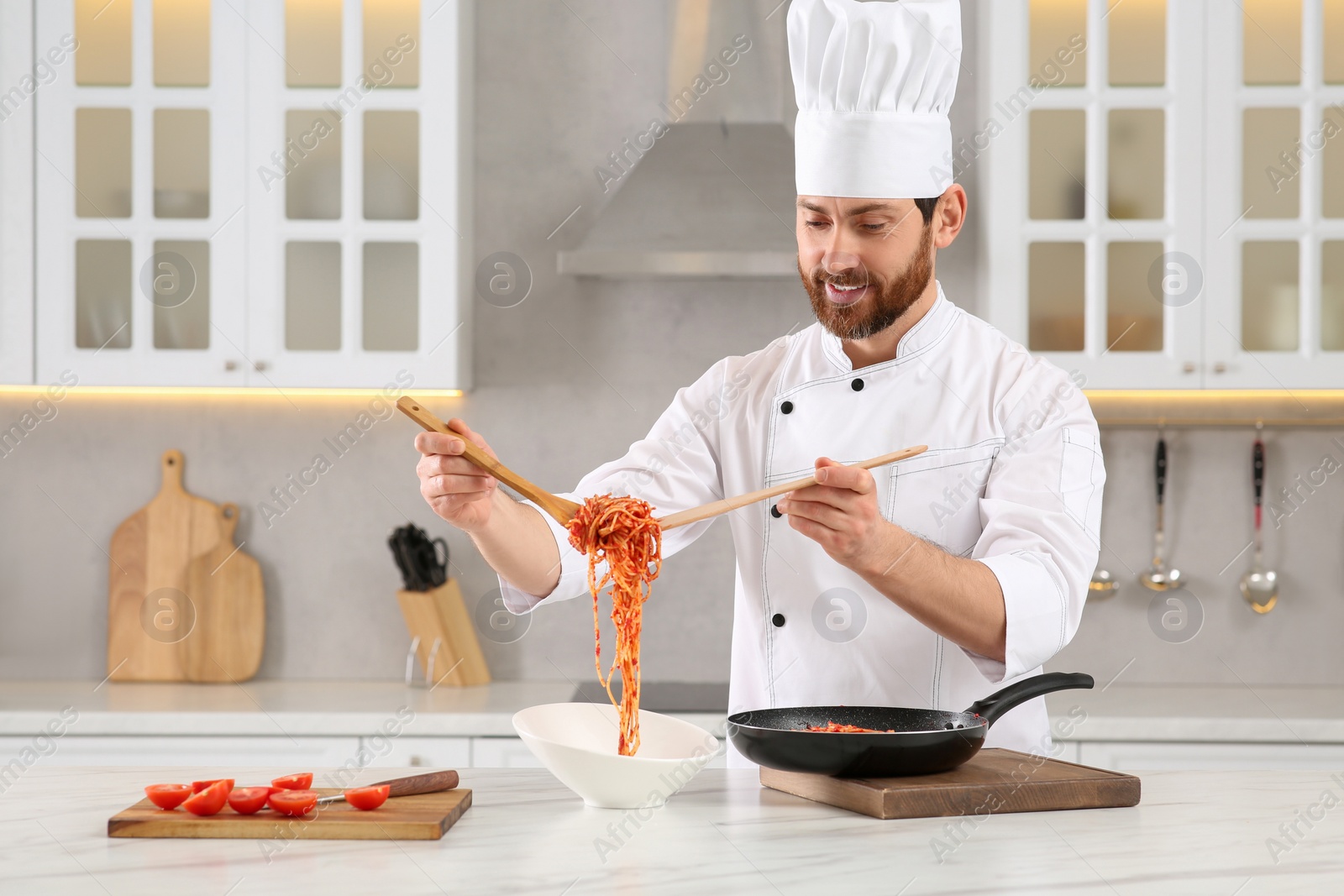 Photo of Professional chef putting delicious spaghetti into bowl at marble table in kitchen