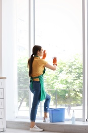 Photo of Young woman cleaning window glass at home