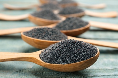 Poppy seeds in spoons on blue wooden table, closeup