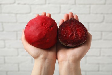 Photo of Woman holding dough painted with natural food coloring and beet near white brick wall, closeup