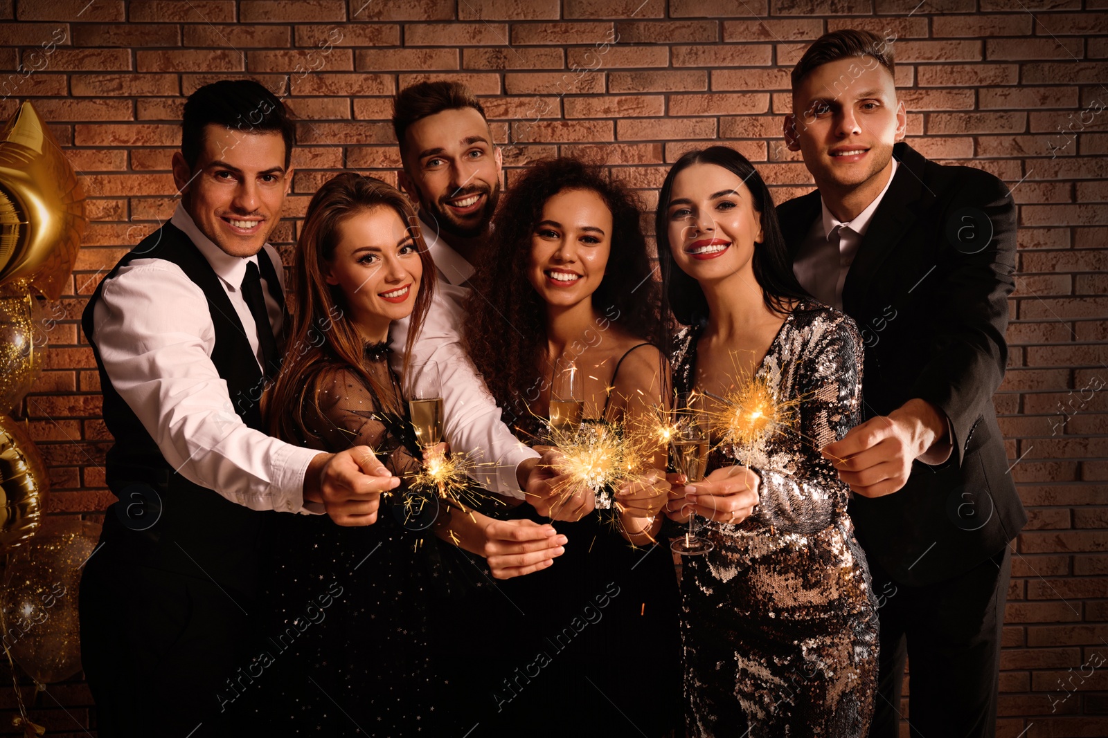 Photo of Happy friends with glasses of sparkling wine and sparklers celebrating New Year indoors