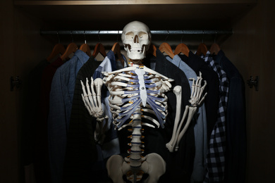 Photo of Artificial human skeleton model among clothes in wardrobe