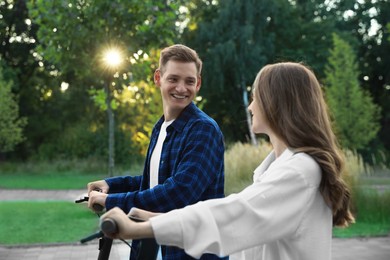 Photo of Happy couple riding modern electric kick scooters in park