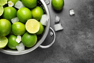 Photo of Colander with fresh ripe limes and ice cubes on gray background, top view