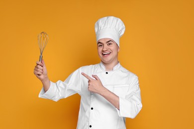 Photo of Portrait of happy confectioner in uniform holding whisk on orange background