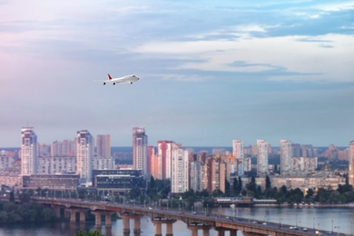 Image of Modern airplane flying in cloudy sky over city