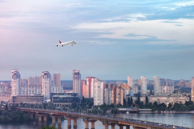 Modern airplane flying in cloudy sky over city