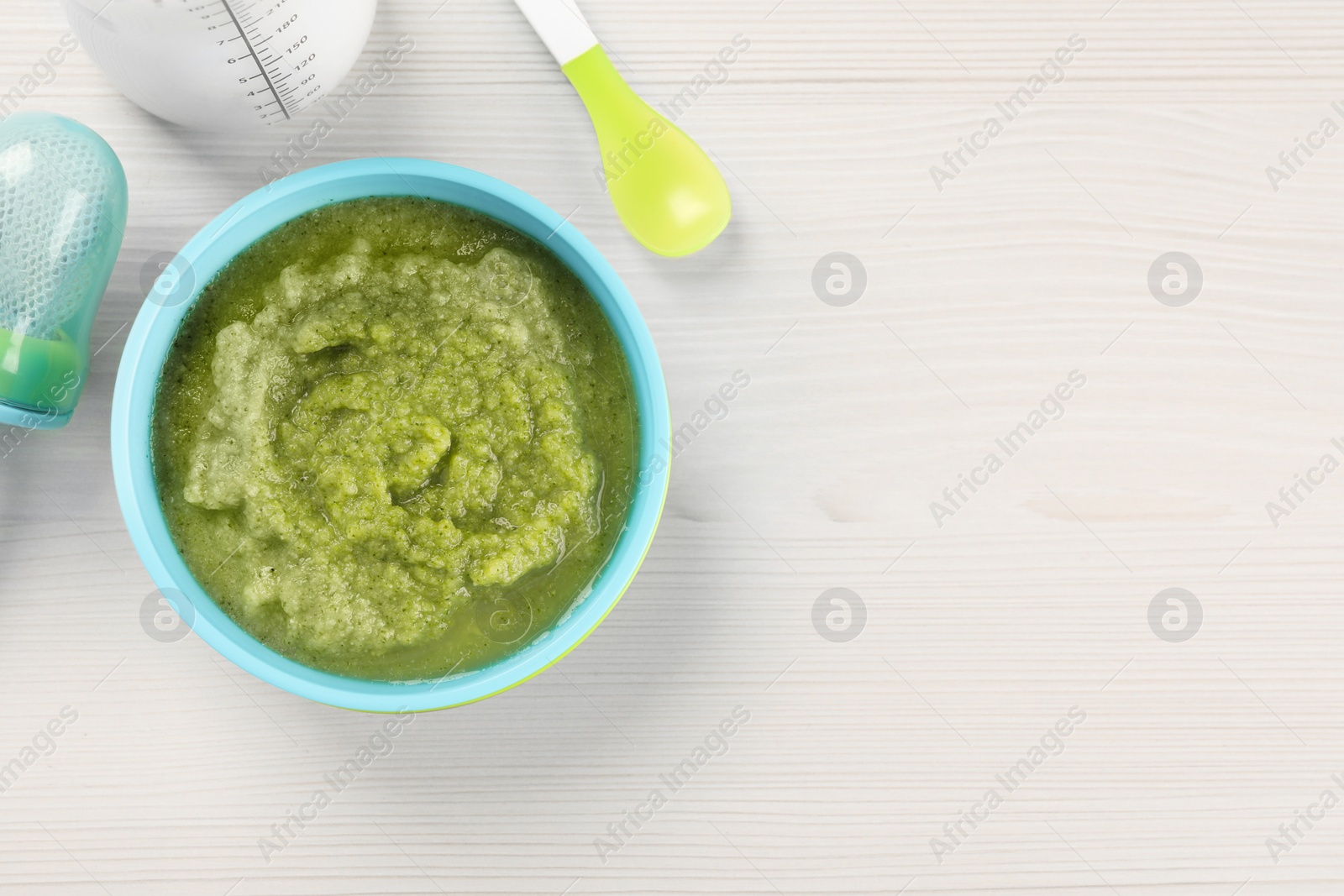 Photo of Healthy baby food. Bowl with tasty broccoli puree on white wooden table, flat lay and space for text
