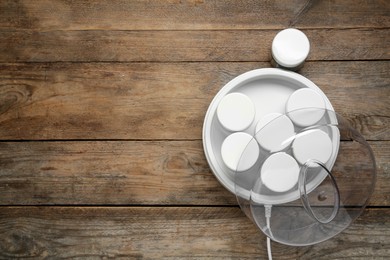 Photo of Modern yogurt maker with jars on wooden table, flat lay. Space for text