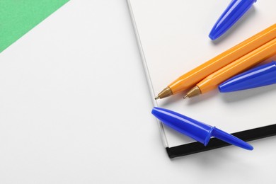 Photo of Ballpoint pens and notebook on white background, top view. Space for text