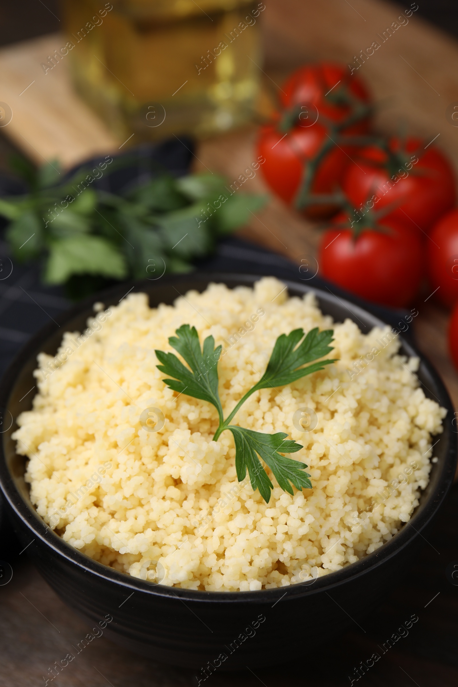 Photo of Tasty couscous and fresh parsley in bowl on table, closeup