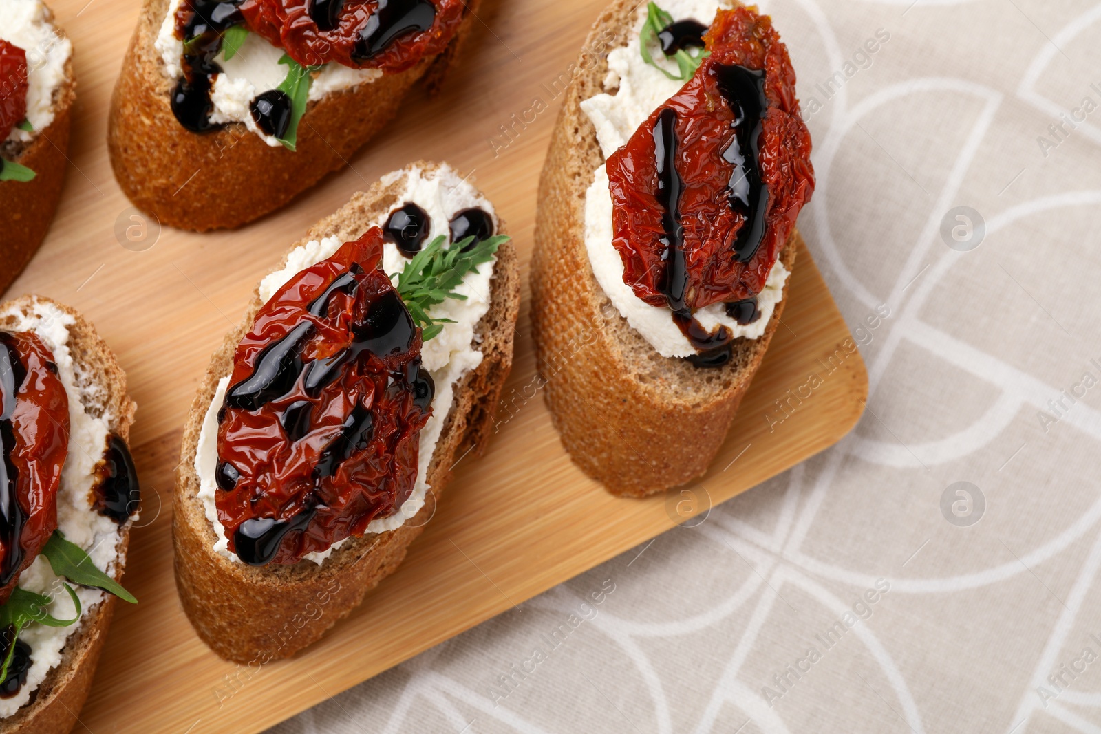 Photo of Delicious bruschettas with sun-dried tomatoes, cream cheese and balsamic vinegar on beige table, top view