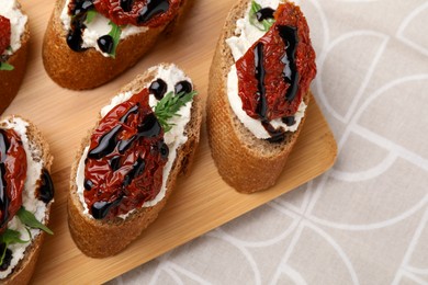 Photo of Delicious bruschettas with sun-dried tomatoes, cream cheese and balsamic vinegar on beige table, top view