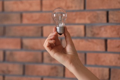 Photo of Woman holding light bulb near brick wall indoors, closeup