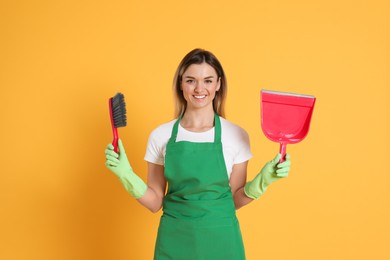 Young woman with broom and dustpan on orange background