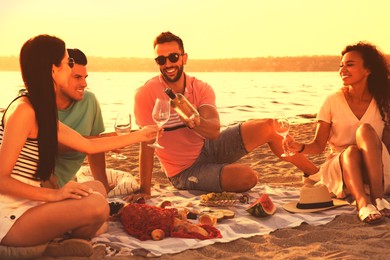Image of Group of friends having picnic outdoors at sunset