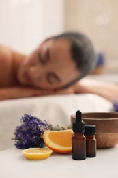 Photo of Woman relaxing on massage couch and bottles of essential oil with ingredients on table in spa salon, selective focus