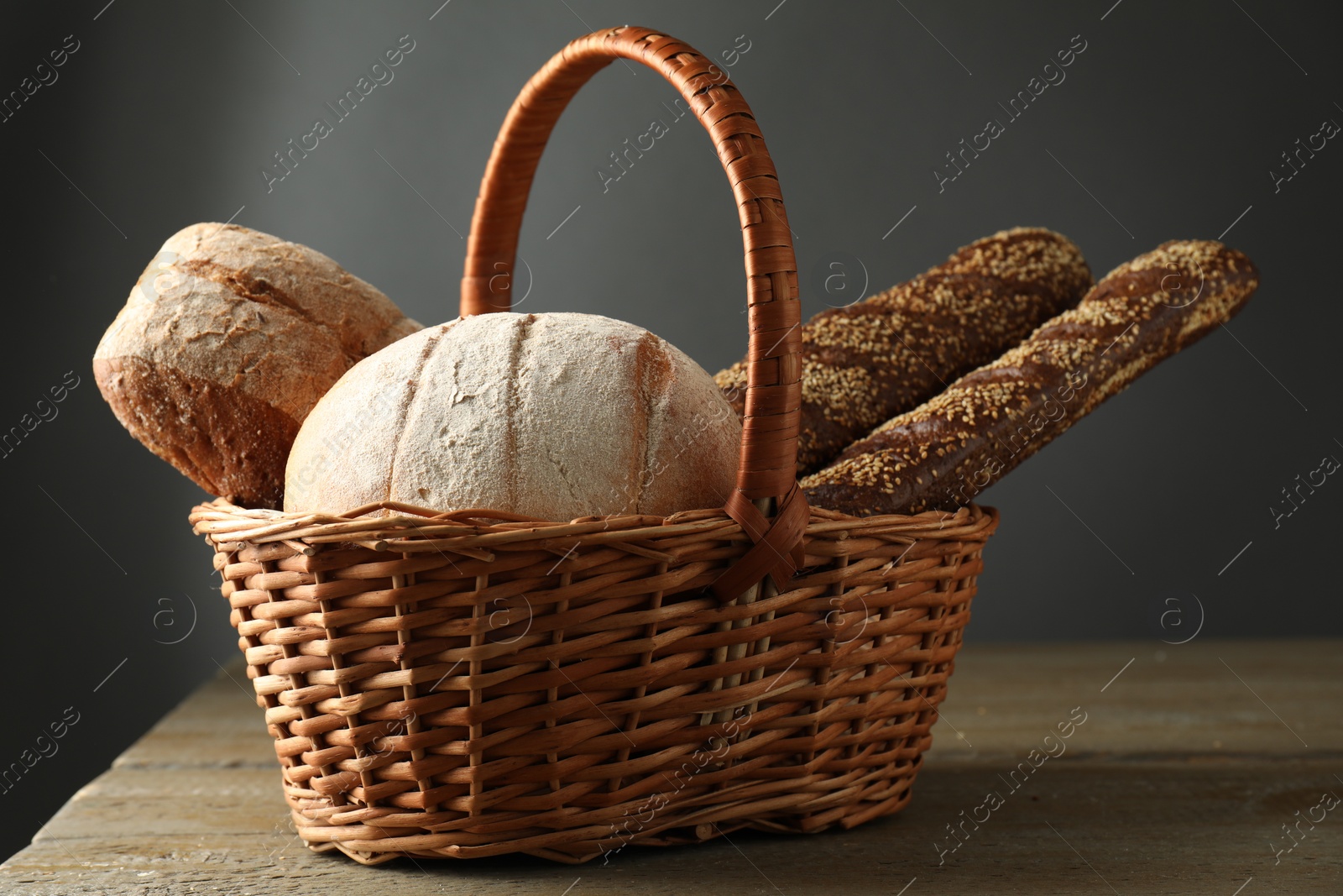 Photo of Wicker basket with different types of fresh bread on wooden table