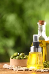 Photo of Bottles with cooking oil, olives and rosemary on wooden table against blurred background