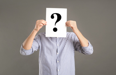 Man holding paper with question mark on grey background