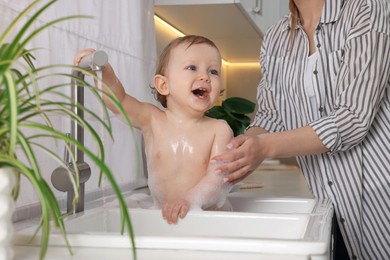 Mother washing her little baby in sink at home