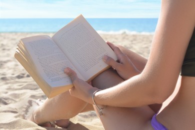 Photo of Woman reading book on sandy beach near sea, closeup