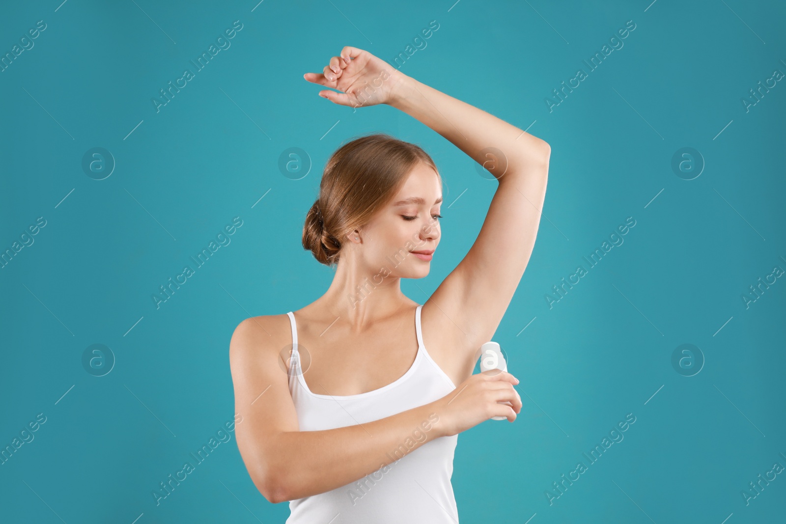 Photo of Young woman applying deodorant to armpit on teal background