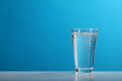 Glass of soda water on light blue background, space for text