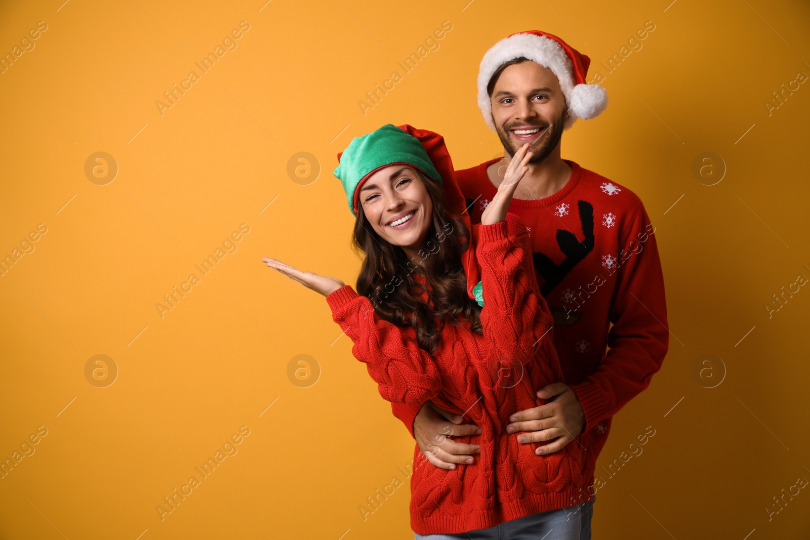 Photo of Young couple in Christmas sweaters and hats on yellow background. Space for text