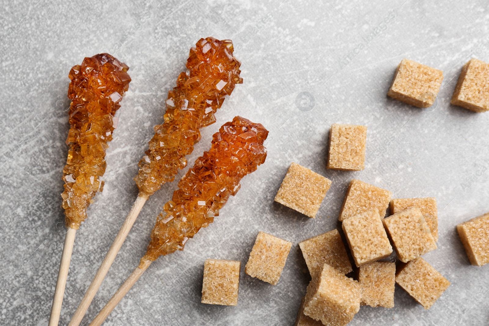 Photo of Wooden sticks with sugar crystals and cubes on light grey table, flat lay. Tasty rock candies